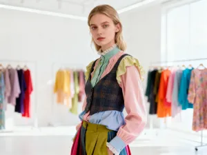 Stylowe botki zestawione z plisowaną spódnicą i wełnianym płaszczem na tle jesiennej ulicy z opadłymi liśćmi.